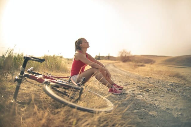 Girl with bike sitting near the road